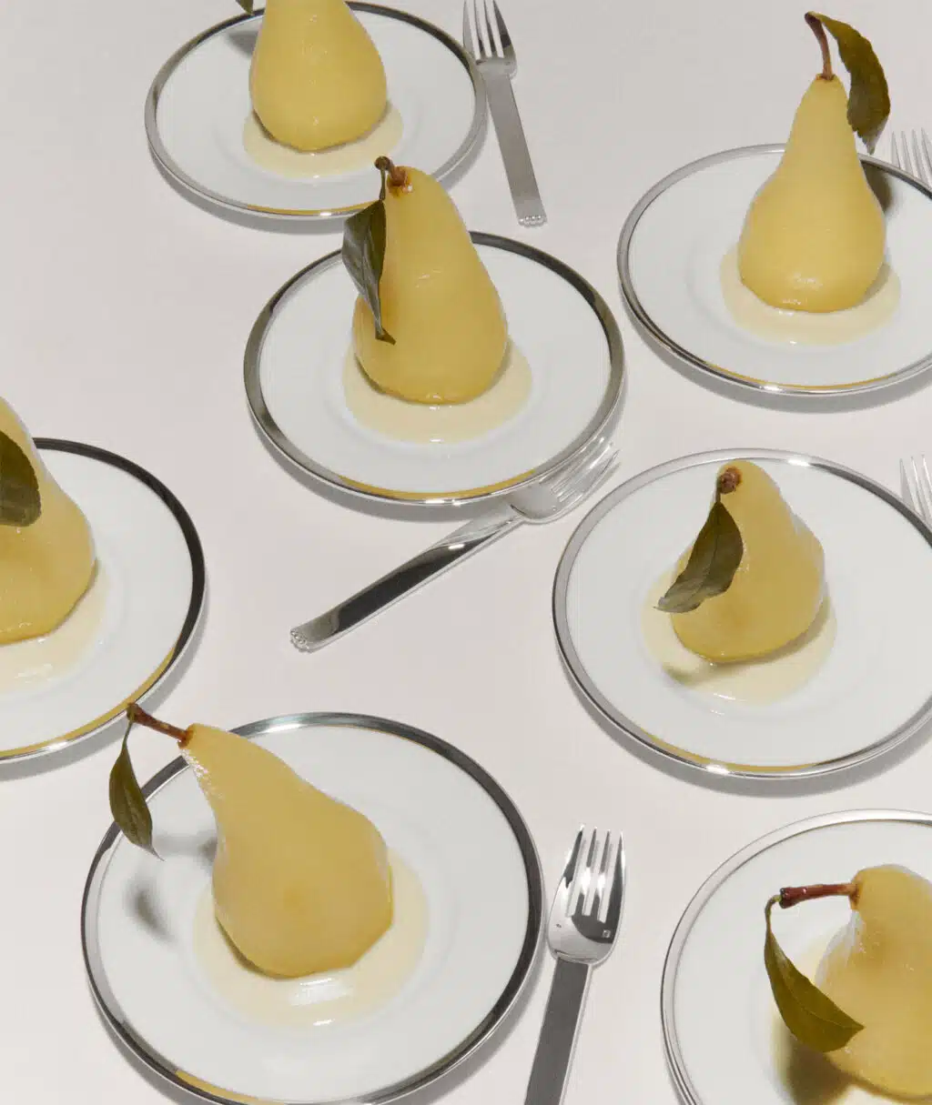 Assiettes Cercle d'Orfèvre et fourchettes Deauville dressées avec des poires pochées sur une nappe blanche