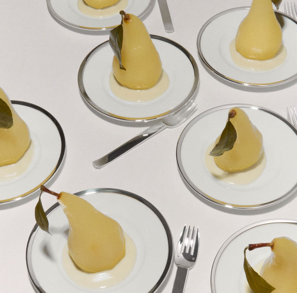 Assiettes Cercle d'Orfèvre et fourchettes Deauville dressées avec des poires pochées sur une nappe blanche